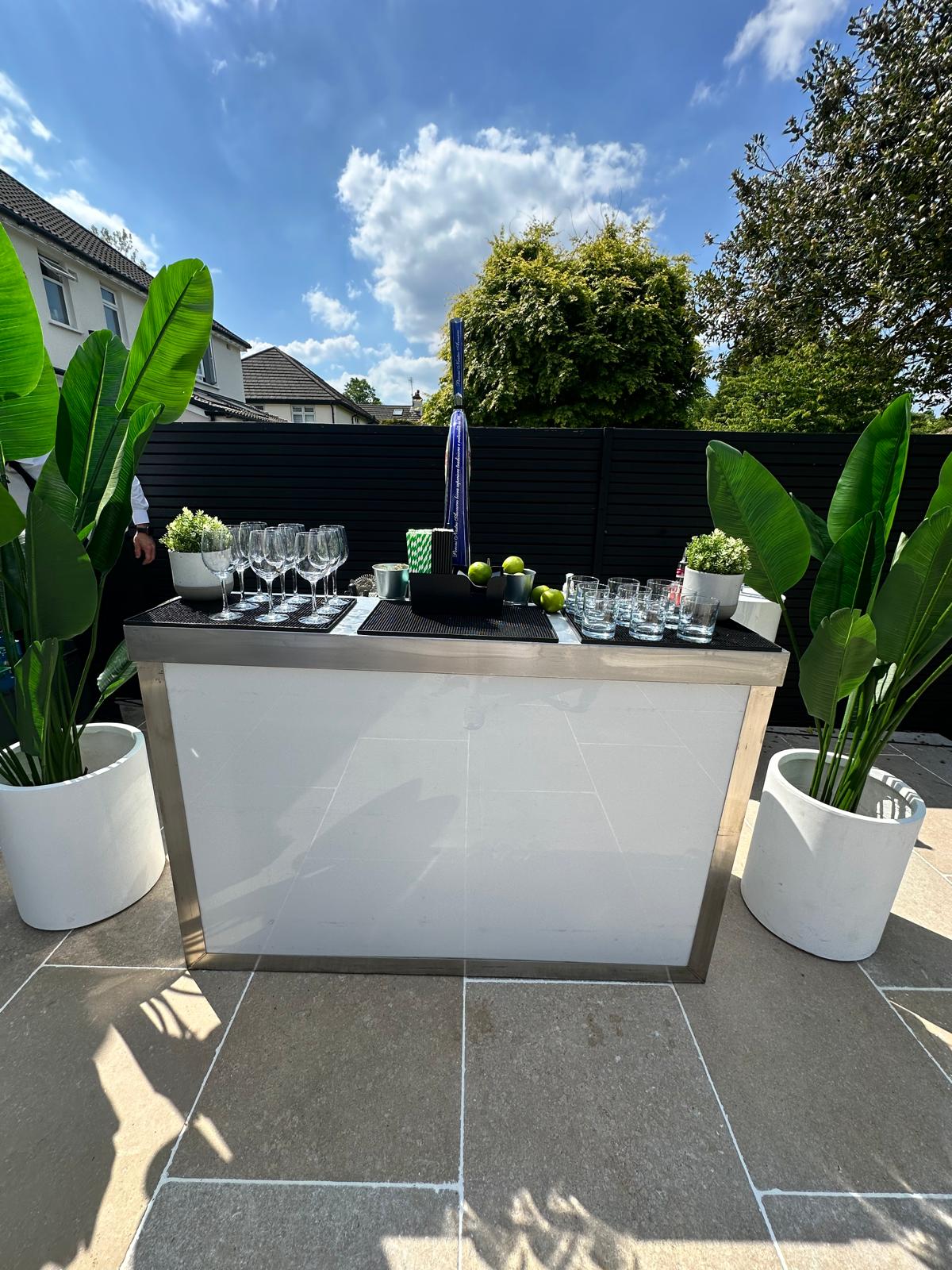 Mirror-finish mobile bar set up outdoors with tropical planters and stemware